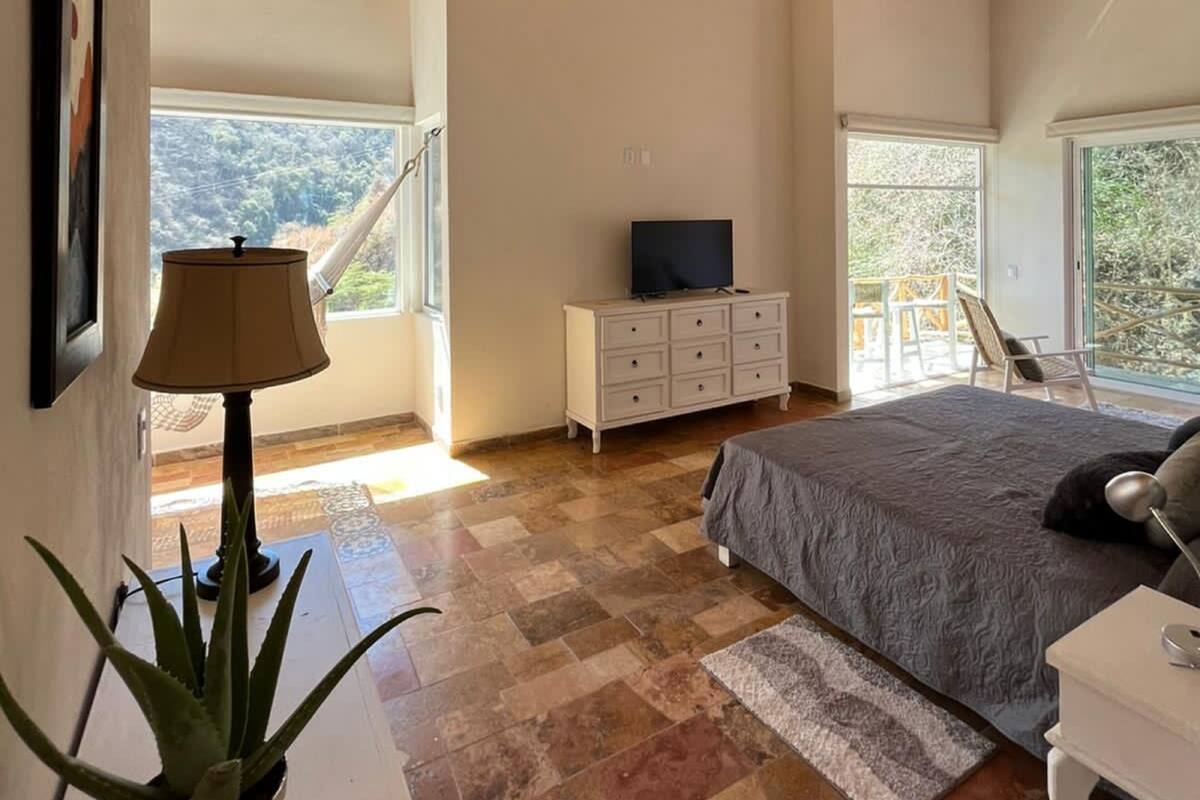 A bedroom with a large bed, a TV on a dresser, and a view of the outdoors through a window.