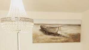 Ein Zimmer mit einem Chandelier, einem Gemälde eines Bootes, einem Sessel und einer Topfpflanze.
