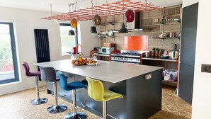 A modern kitchen with a central island, bar stools, hanging pendant lights, and a red ceiling grid. - Luxurious Designer Penthouse - Grand Bay Views (Poole)