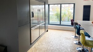 A modern kitchen with a large refrigerator, a dining table with colorful chairs, and a sliding glass door leading to a balcony. - Luxurious Designer Penthouse - Grand Bay Views (Poole)