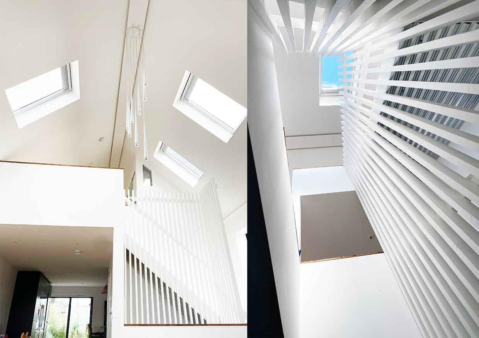 Un interior moderno con techo alto, tragaluces y una escalera con barandillas blancas.