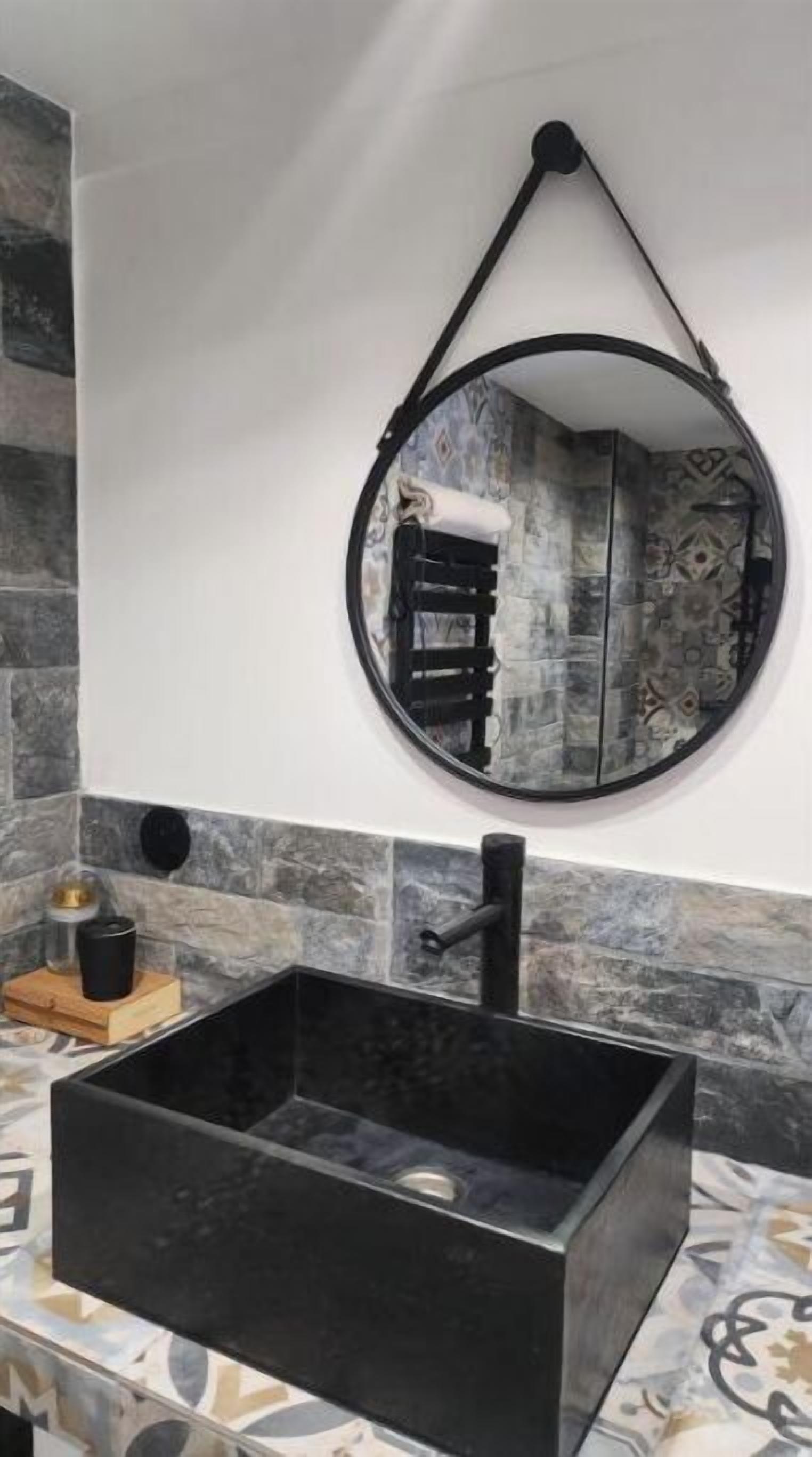 Une salle de bain avec un lavabo rectangulaire noir, un miroir rond et un porte-serviettes.