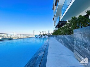 A modern rooftop pool with clear blue water, a city skyline in the background, and a view of the bridge. - Wonderful 2B With Breathtaking View in JVC (Dubai)