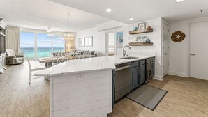 A modern kitchen with a large island, a dining area with a view, and a living room with a sofa and a coffee table. - WaveSong: Luxurious Beachfront Condo at Navarre Beach. Sleeps 9 (Navarre)