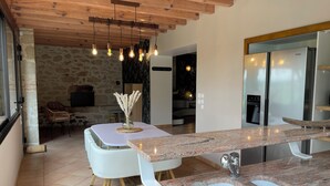 Una cocina moderna con encimeras de granito, un refrigerador de acero inoxidable y un comedor con sillas blancas, con una pared de piedra de fondo.