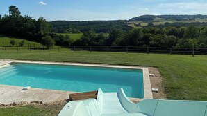 Una piscina con tobogán, rodeada de césped y una cerca, con vistas a colinas onduladas al fondo.