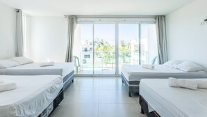 Een hotelkamer met twee bedden, een balkon en uitzicht op gebouwen en groen.