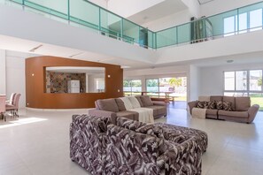 Amplia sala de estar con techo alto, balcón con barandilla de cristal y vistas al exterior.