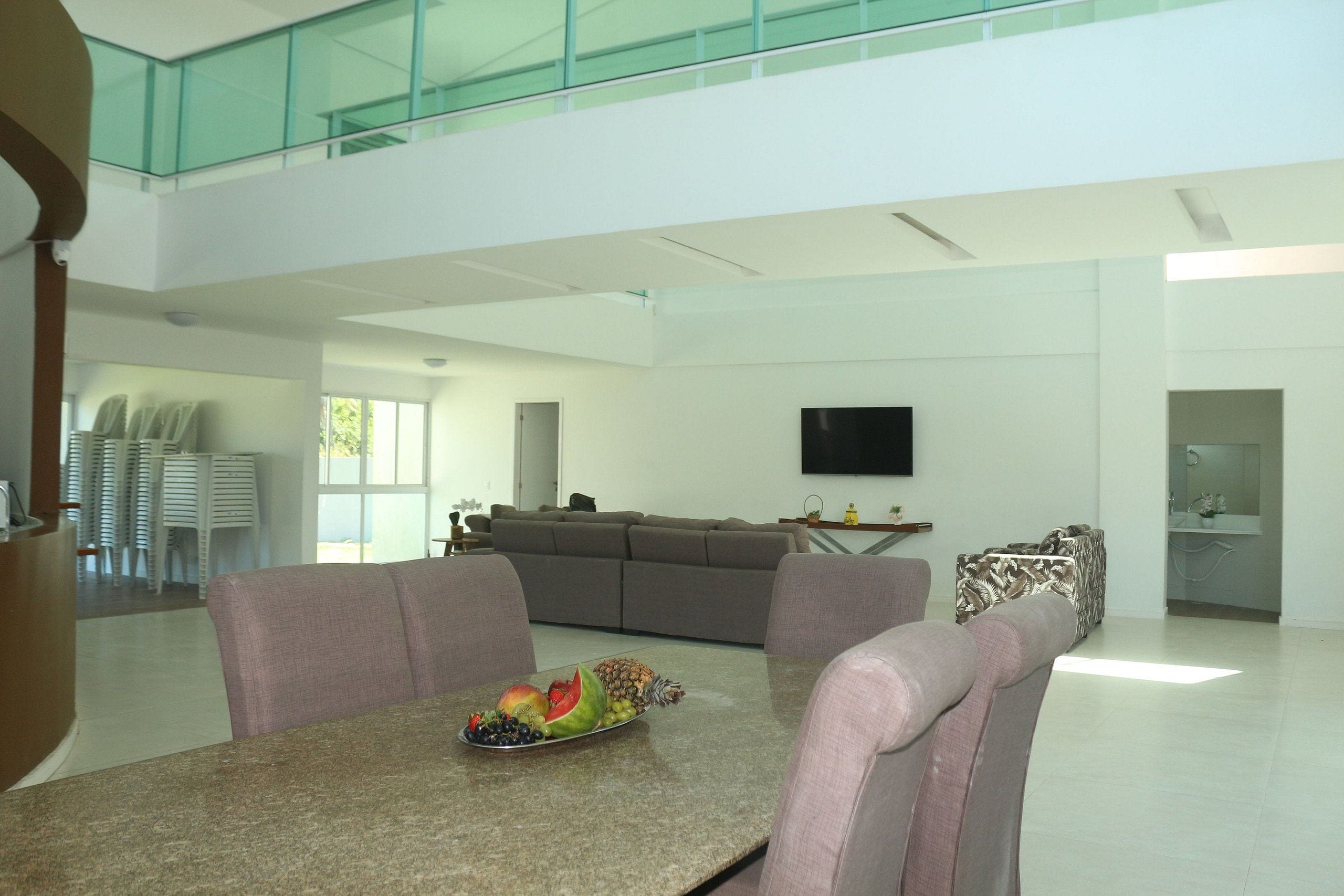 A spacious living area with a dining table set with fruit, a grey sofa, and a television mounted on the wall.