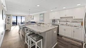 Une cuisine moderne avec des meubles blancs, un grand îlot central doté de tabourets et une vue sur l’extérieur.