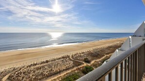 Une vue sur la plage depuis un balcon, avec un ciel dégagé et un soleil éclatant.