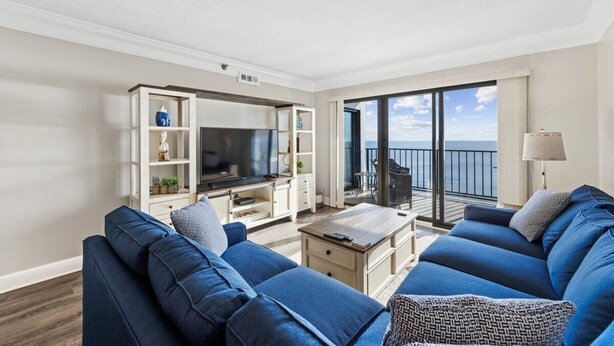 Un salon moderne avec une grande télévision, des canapés bleus, une table basse et un balcon offrant une belle vue.