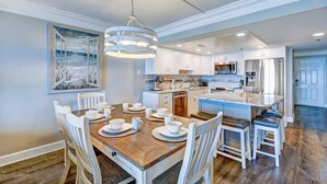 Une cuisine moderne avec des meubles blancs, un îlot central et un coin repas comprenant une table en bois et des chaises blanches.
