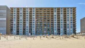 A multi-story hotel with a grid of balconies and a sandy beach in the foreground. - Luxe Oceanfront 1BR | Pool, Hot Tub, Sun Deck (Ocean City)