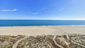 A beach with a clear sky, a sandy shore, and a fence in the foreground. - Luxe Oceanfront 1BR | Pool, Hot Tub, Sun Deck (Ocean City)