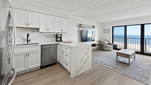 A modern kitchen with white cabinetry, a built-in dishwasher, and a large island with a marble countertop. - Luxe Oceanfront 1BR | Pool, Hot Tub, Sun Deck (Ocean City)