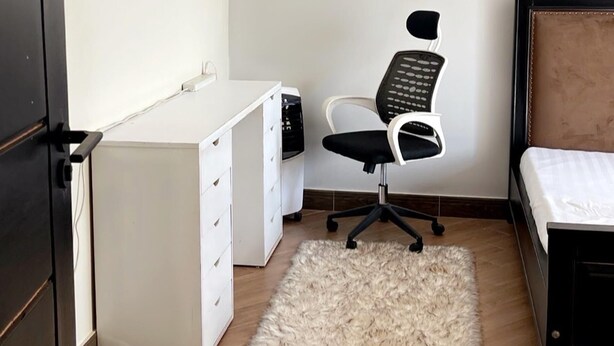 A bedroom with a bed, a desk with drawers, a chair, and a fluffy rug. - 1 Bed Flat - Sleeps 2 - Parking - Wifi (Kampala)