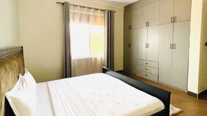 A bedroom with a bed, a wardrobe, and a window with curtains. - 1 Bed Flat - Sleeps 2 - Parking - Wifi (Kampala)