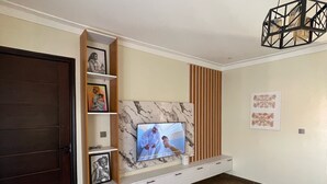 A living room with a TV, wooden panel wall, and a dark door. - 1 Bed Flat - Sleeps 2 - Parking - Wifi (Kampala)