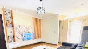 A modern living room with a sectional sofa, a white coffee table, and a marble accent wall. - 1 Bed Flat - Sleeps 2 - Parking - Wifi (Kampala)