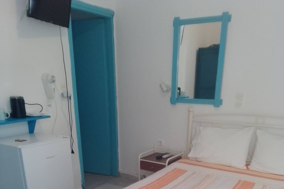 A bedroom with a bed, a bedside table, a desk, and a mirror on the wall.