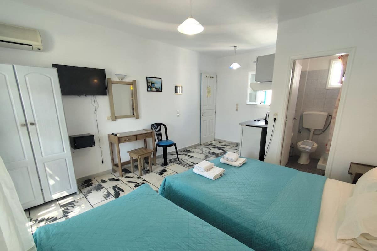 A hotel room with two beds, a desk, a chair, a TV, a mirror, and a bathroom.