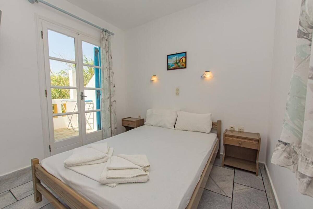 A bedroom with a bed, two bedside tables, a painting on the wall, and a door leading to an outdoor area.