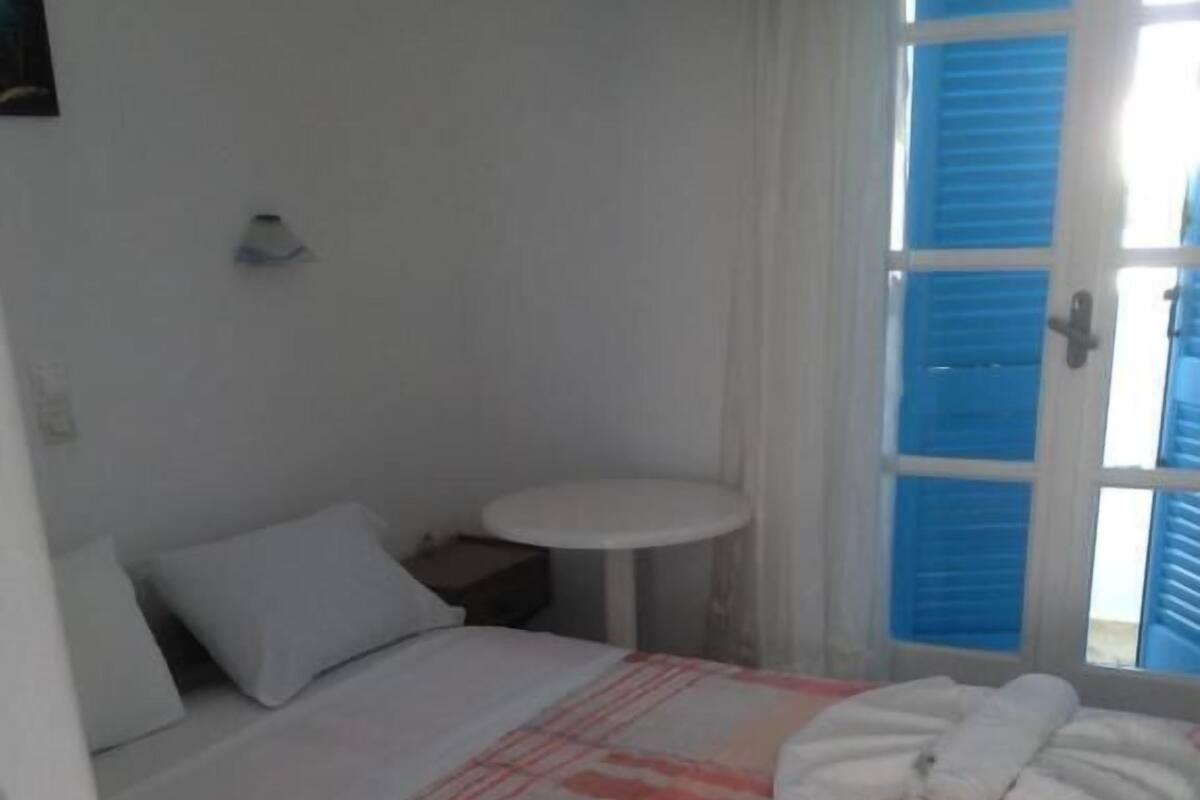 A hotel room with a bed, a small round table, and a window with blue shutters.