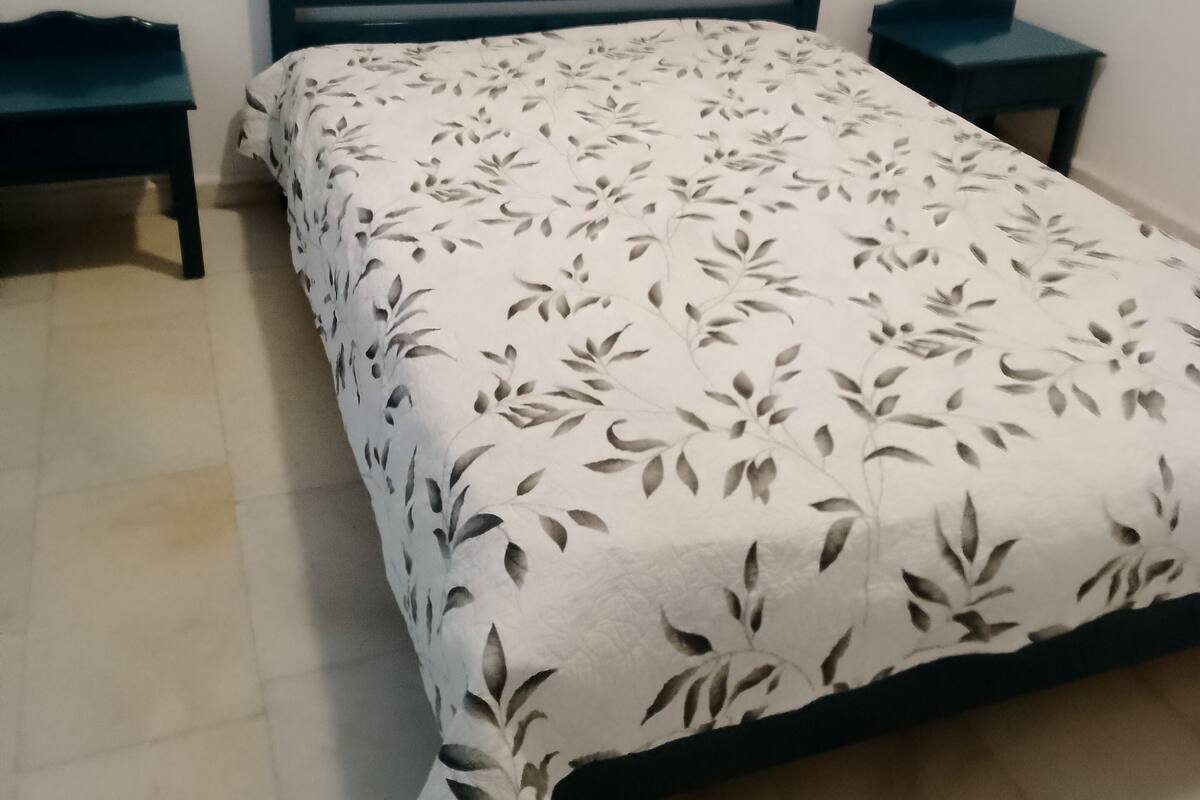 A bedroom with a bed, two nightstands, a window with curtains, and a tiled floor.