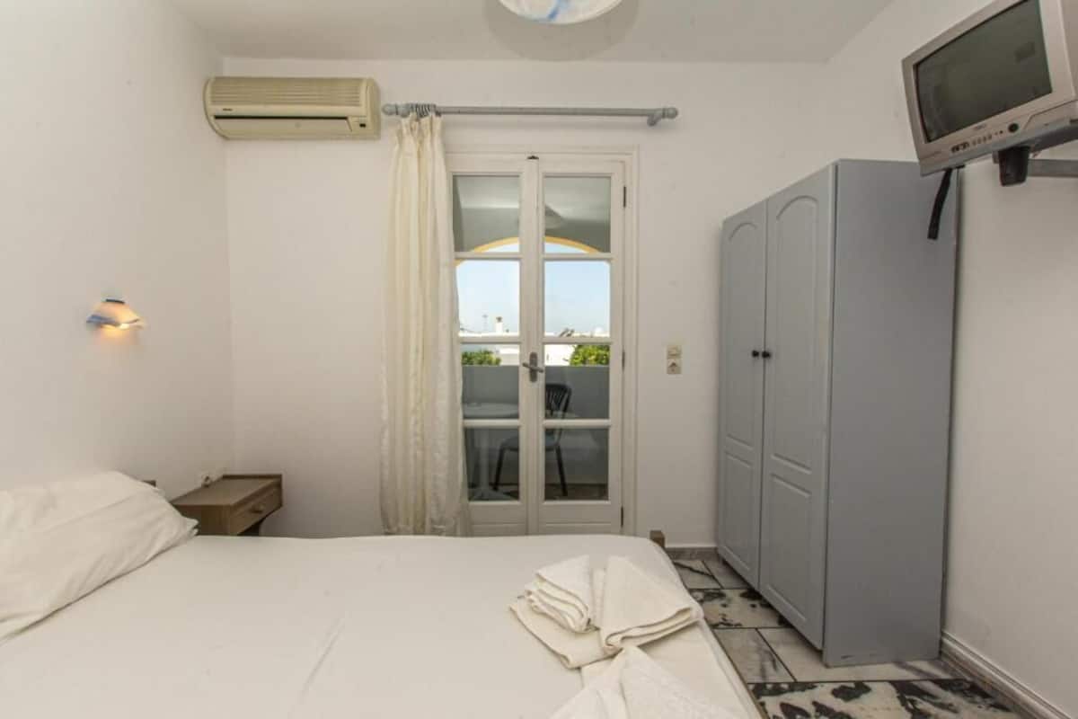 A bedroom with a bed, a wardrobe, an air conditioning unit, a television, and a window with curtains.