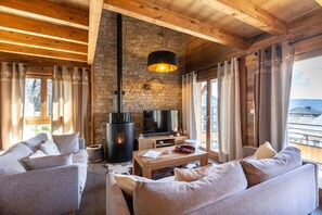 A cozy living room with a stone wall, wooden ceiling, and a fireplace. There is a sofa, a coffee table, and a TV. - Les Chevreaux - Chalet avec vue montagne (Font-Romeu)