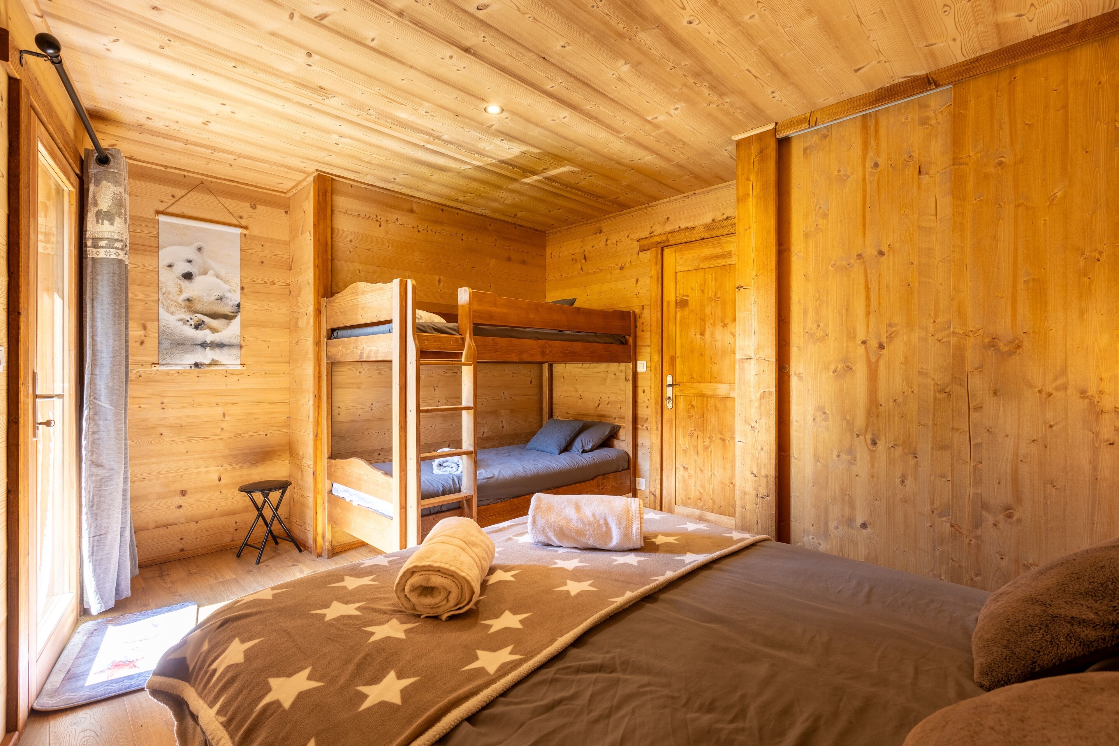 A wooden cabin room with bunk beds, a star-patterned bedspread, and a framed picture on the wall.