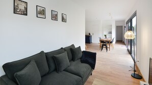 Ein modernes Wohnzimmer mit einem dunkelgrünen Sofa, einem Essbereich mit Tisch und Stühlen und einem großen Fenster mit Stehlampe.