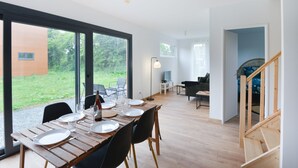 Ein moderner Essbereich mit einem Holztisch, gedeckt für vier Personen, großen Fenstern und Blick auf einen Garten.