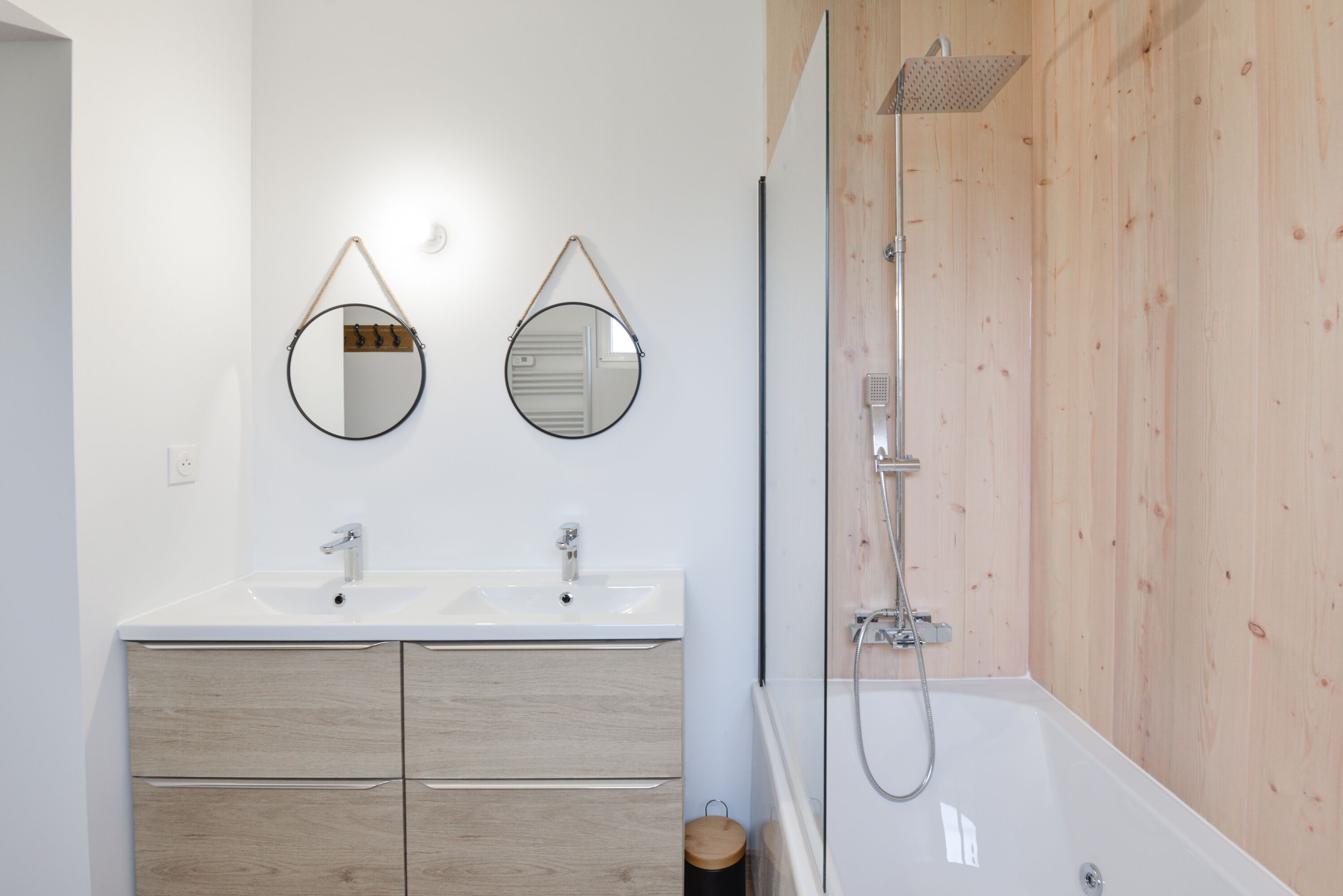 A modern bathroom with two sinks, wooden cabinets, and a glass-enclosed shower.