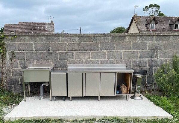 Un espace cuisine extérieur doté d’un mur en pierre, d’un sol en béton et d’un barbecue en métal.