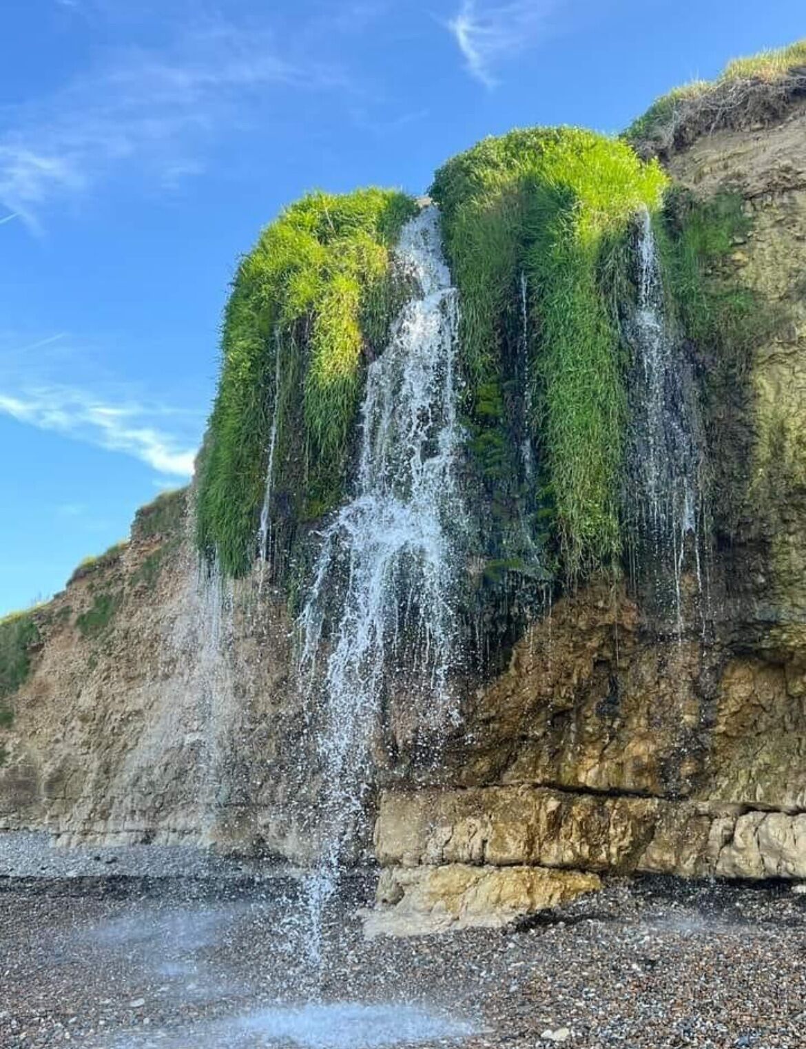 Une cascade se déversant le long d’une falaise rocheuse, avec une végétation luxuriante et verdoyante au sommet.