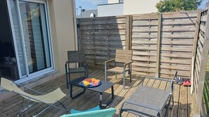 Eine Holzterrasse mit Gartenmöbeln, darunter Stühle und ein Tisch, sowie ein kleiner Tisch mit Obst.