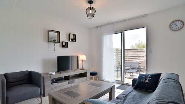 Ein modernes Wohnzimmer mit Flachbildfernseher, Couchtisch, Sofa und einem Essbereich, der durch eine Glasschiebetür sichtbar ist.