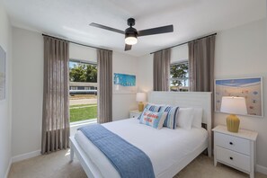 Una camera d'albergo con un letto, una ventola a soffitto, un comodino con una lampada e una finestra con tende.