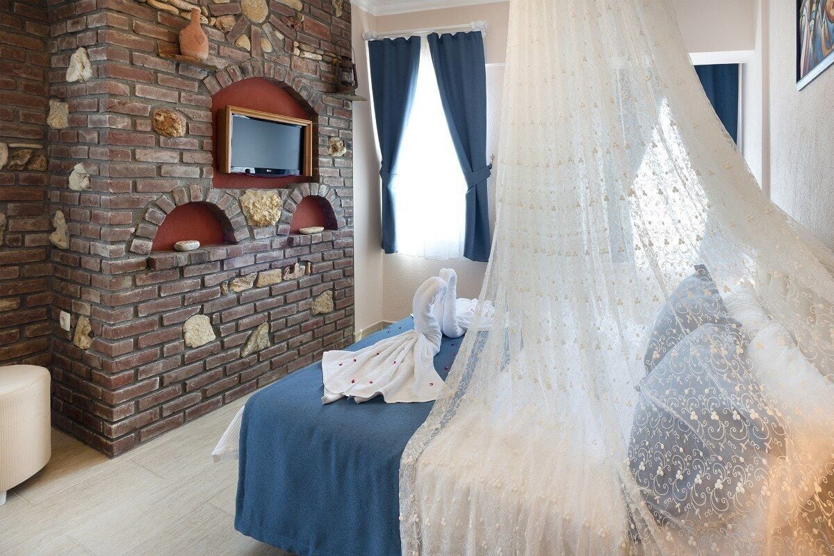 A bedroom with a brick fireplace, a bed with a blue bedspread, and a large window with blue curtains.