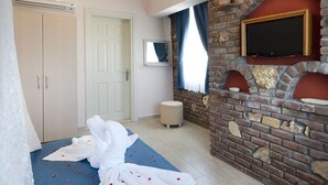 A hotel room with a bed, a TV mounted on a brick wall, a wardrobe, and a small stool. - Begonvil Hotel Bozcaada (Bozcaada)