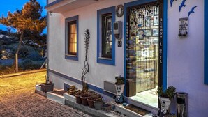 A building with a blue and white facade, a large glass window, and potted plants on the steps. - Begonvil Hotel Bozcaada (Bozcaada)