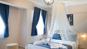 A bedroom with a bed, a canopy, a bedside table, a wall-mounted lamp, and a painting on the wall. - Begonvil Hotel Bozcaada (Bozcaada)
