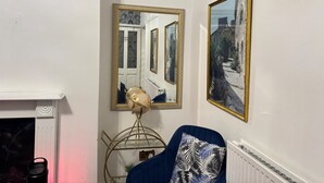 Una habitación con una pared blanca, un globo terráqueo sobre un atril, un sillón azul con un cojín estampado con hojas y dos cuadros enmarcados.