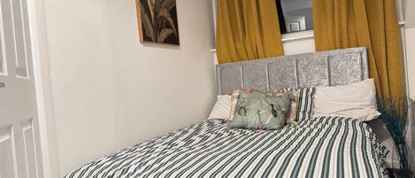 A bedroom with a striped bedspread, a grey headboard, and a window with yellow curtains.
