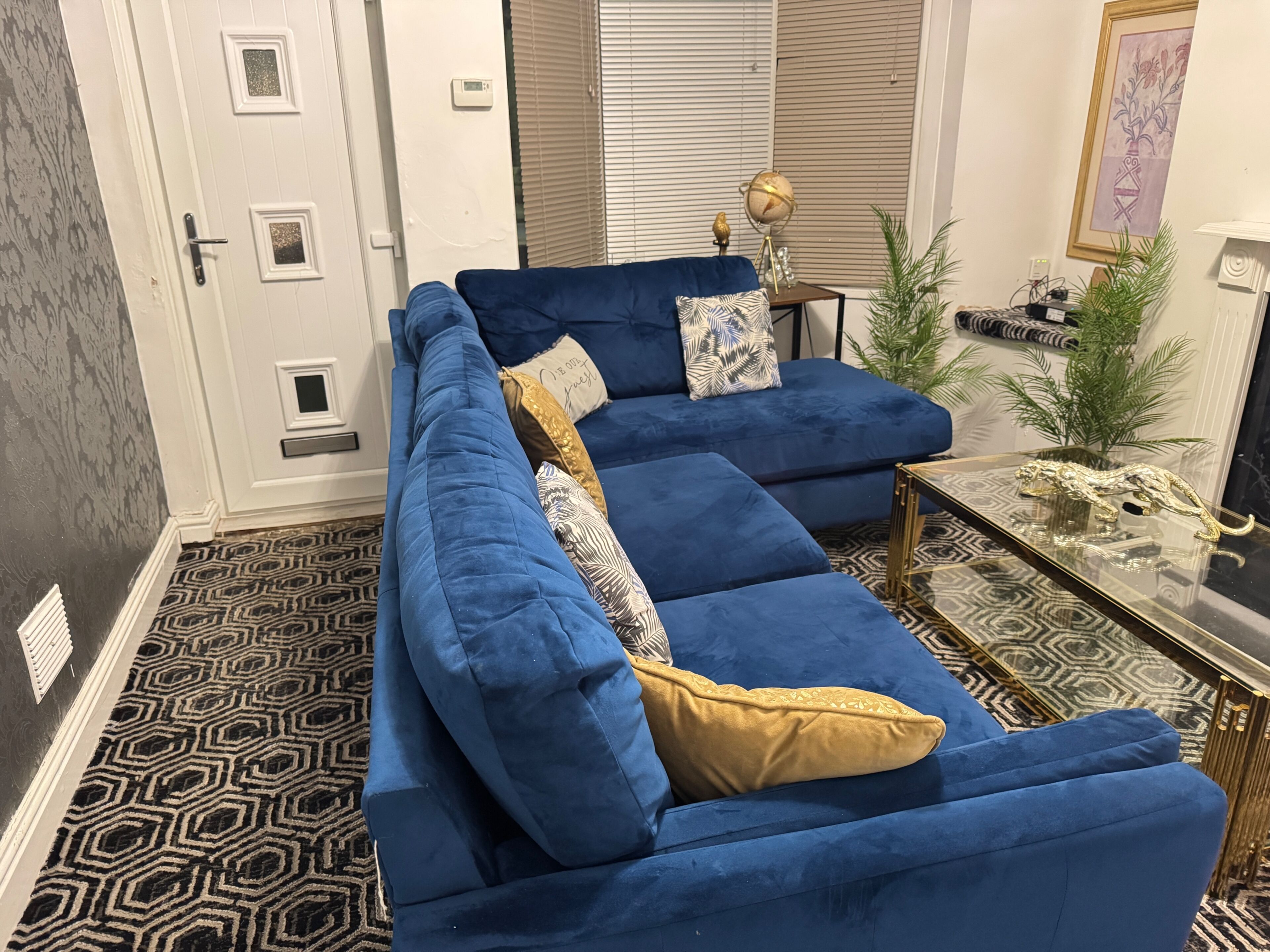 A blue sectional sofa with patterned cushions, a small side table with a globe and decorative items, and a patterned rug on a geometric floor.