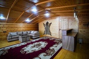 Interior de cabana de madeira com sofá, tapete estampado e pele na parede.