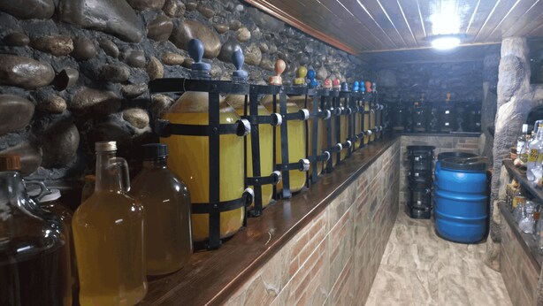 A bar area with stone walls, wooden shelves, and various bottles and containers. - Prestige Guest House (Kutaisi)