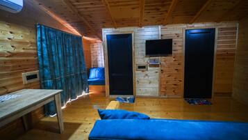 Quarto de cabana de madeira com cama, escrivaninha, televisão e porta.